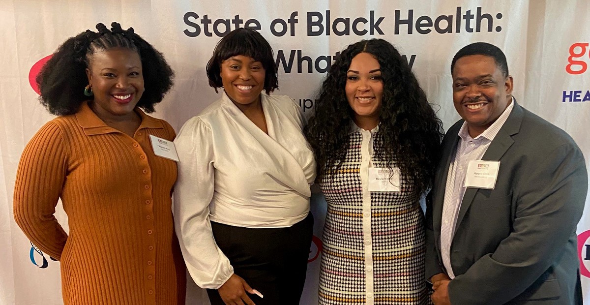Three women and one man standing in front of a step and repeat